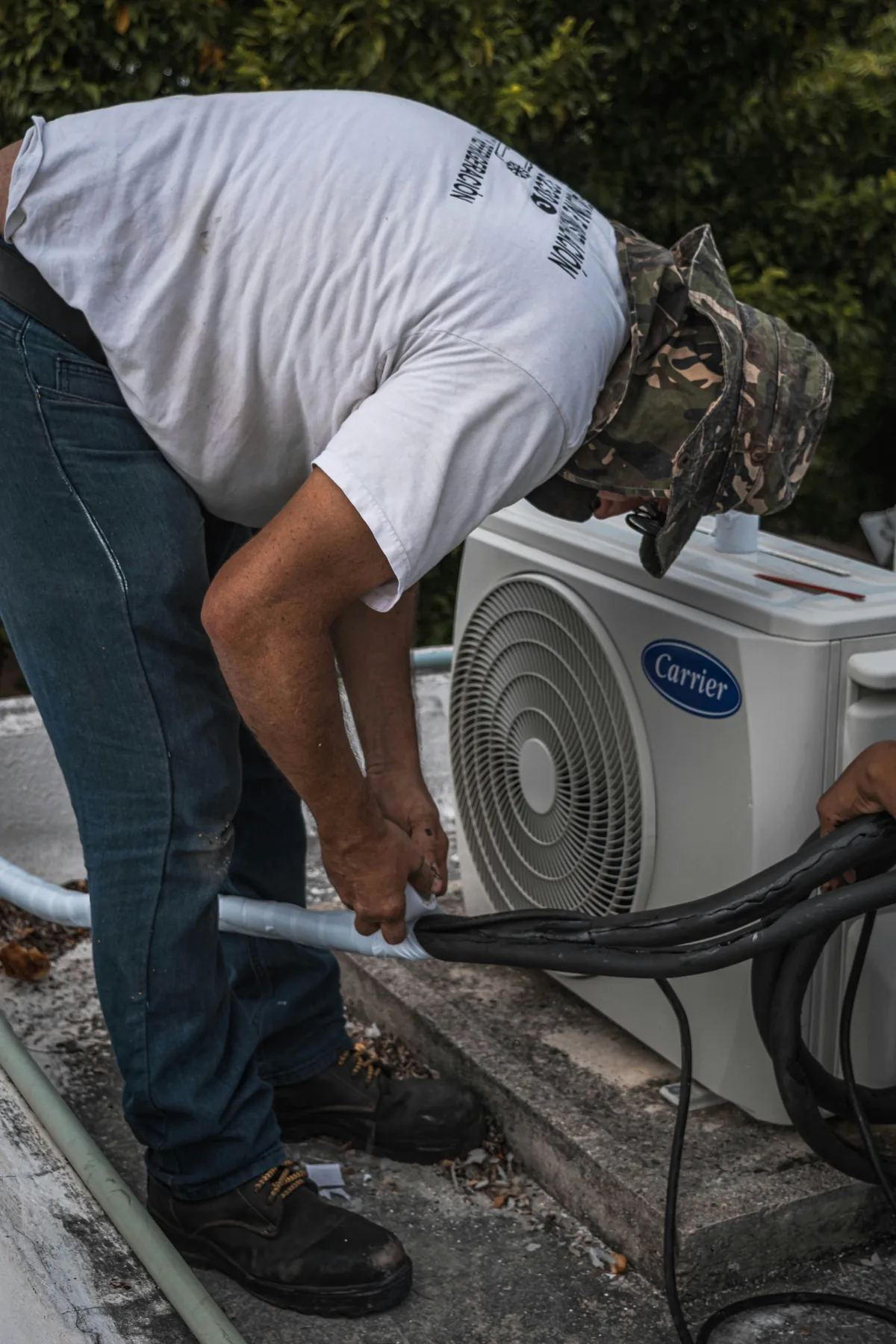 Field HVAC tech repairing the refrigerant line set running into a residential Carrier outdoor unit