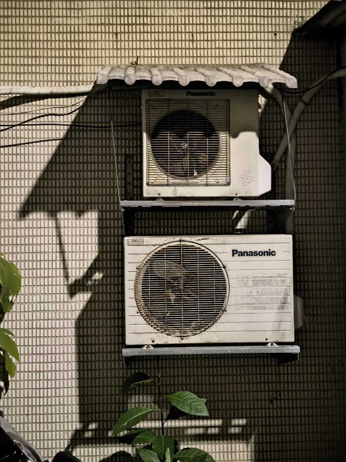 Two aging Panasonic split-system outdoor units stacked on a tiled exterior wall, the kind of older system where compressor failure often pushes the math toward full replacement