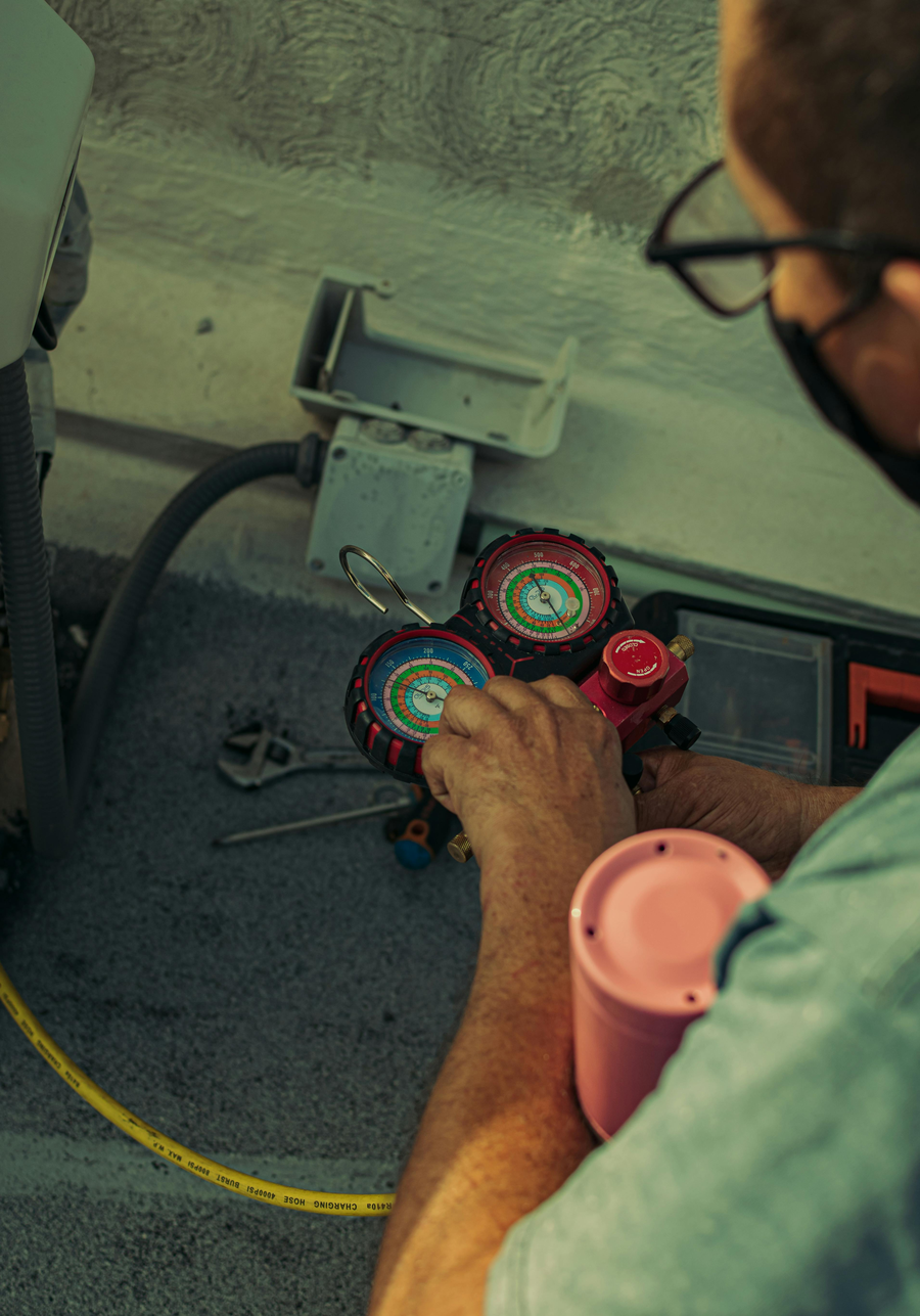 HVAC technician using refrigerant gauges to measure AC system pressure during a tune-up