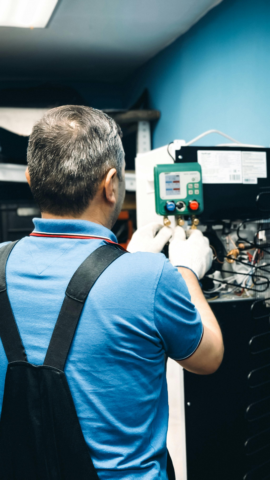 HVAC technician servicing an indoor air handler with gauges connected for refrigerant testing