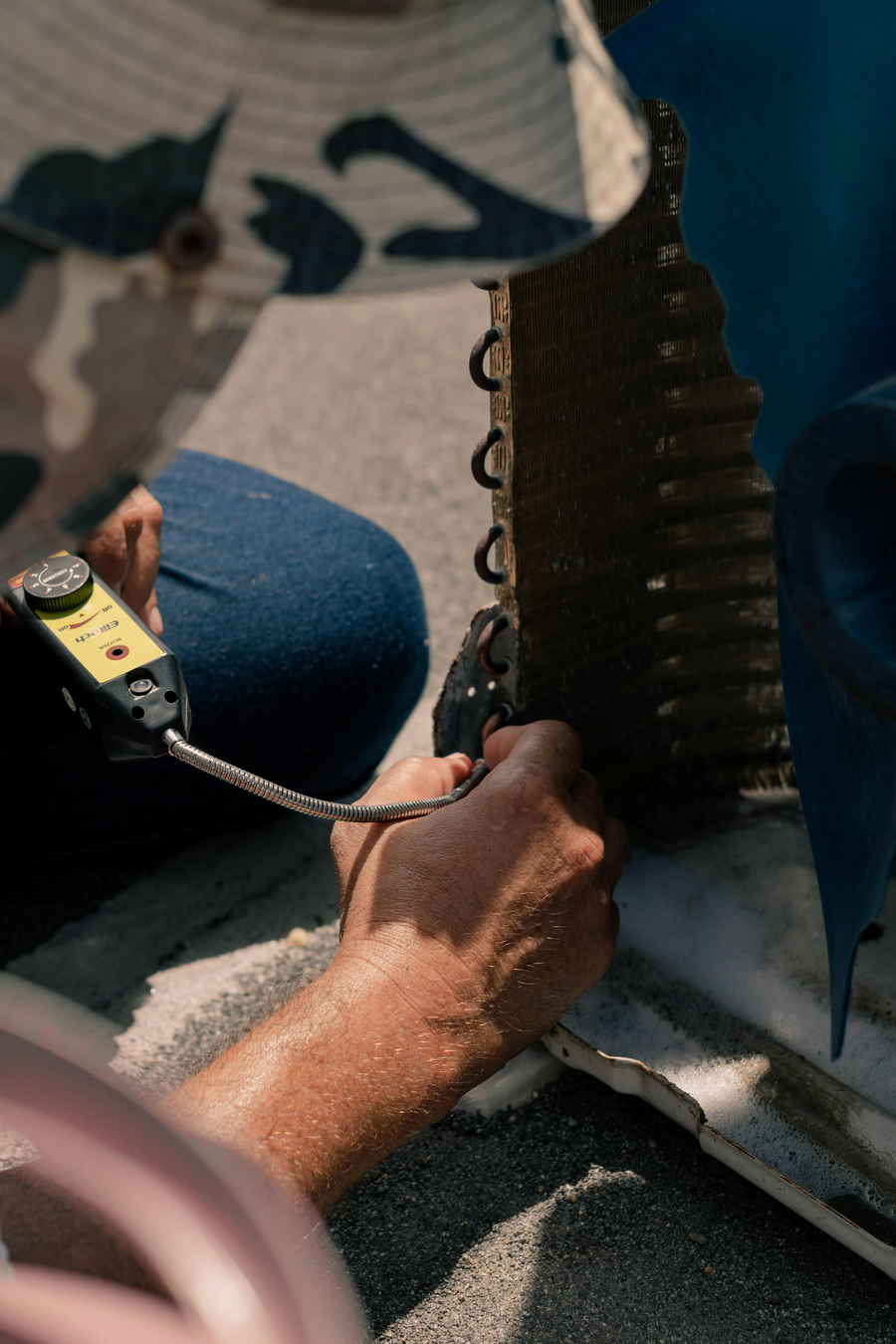 HVAC technician kneeling beside service tools and refrigerant gauges performing an AC tune-up