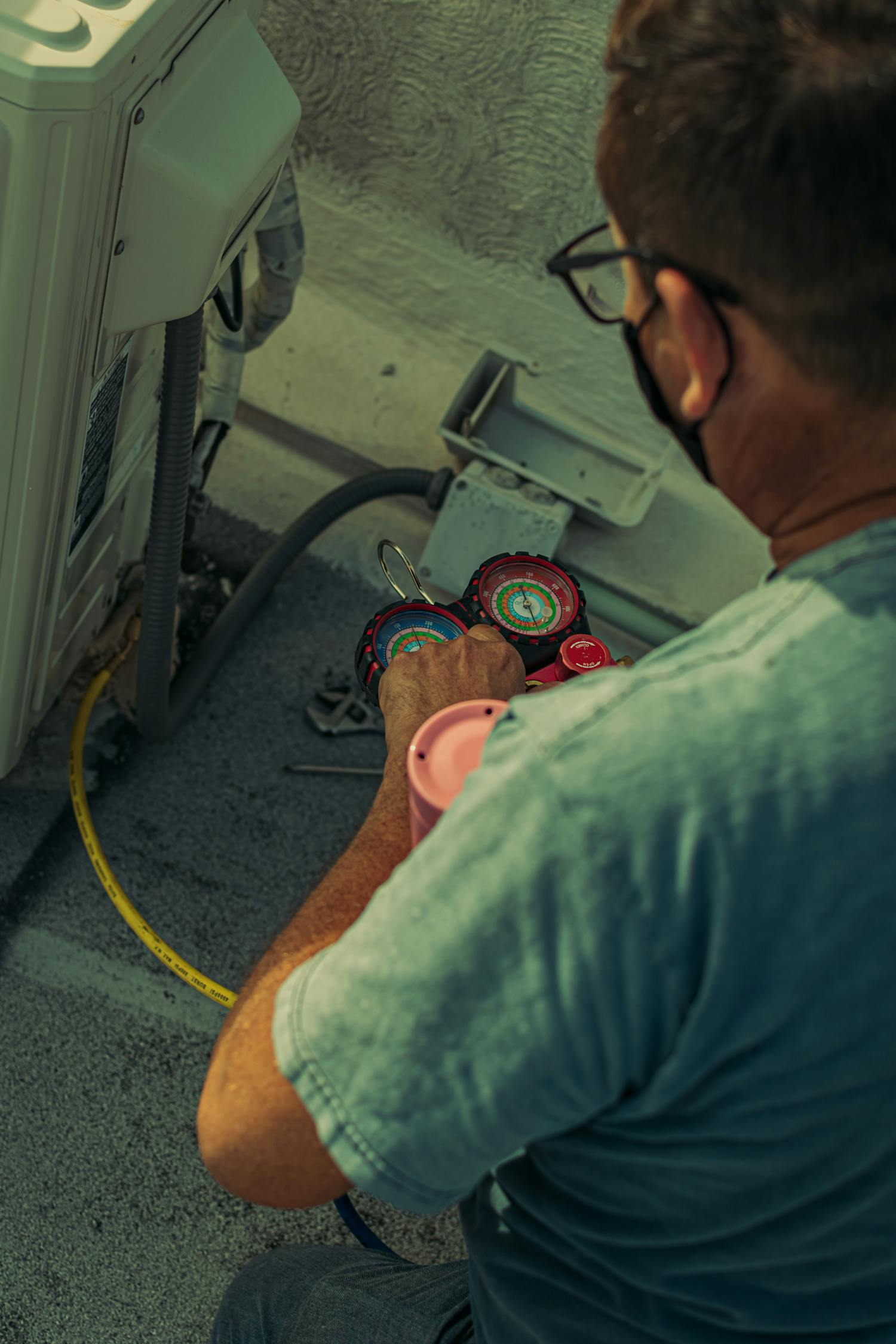 HVAC technician working on a residential air conditioning unit with diagnostic gauges