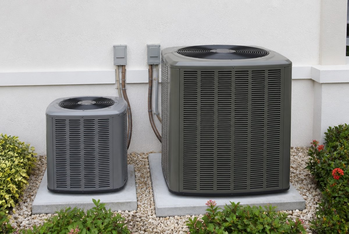 Two outdoor air conditioning condenser units of different sizes side by side on a concrete pad beside a South Florida stucco home