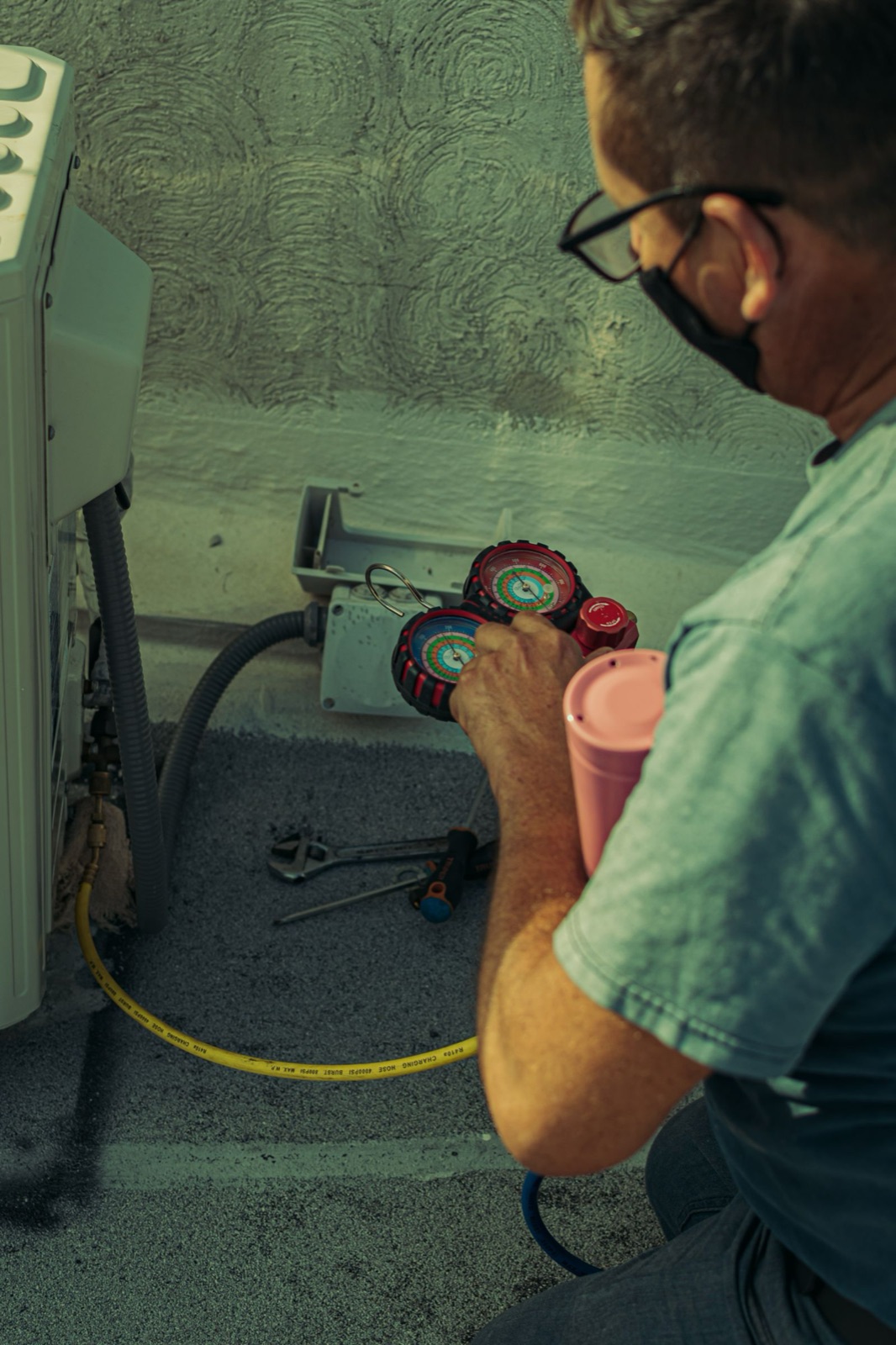 HVAC technician servicing an outdoor AC condenser with refrigerant gauges
