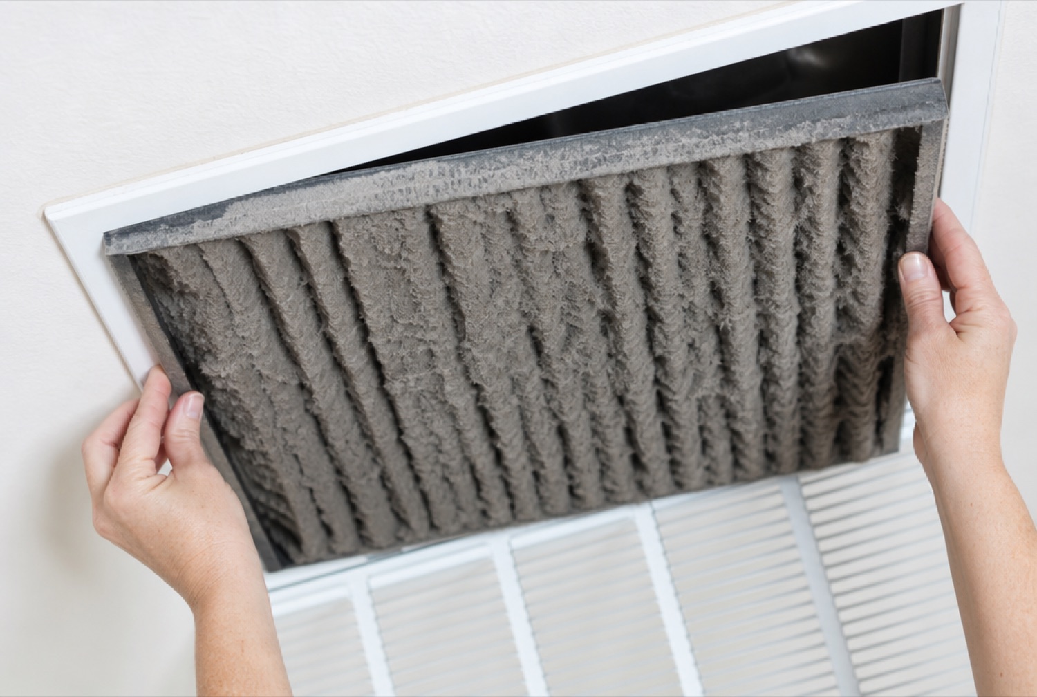 Hands removing a dirty clogged air filter from a return vent, a common reason an AC runs but does not cool
